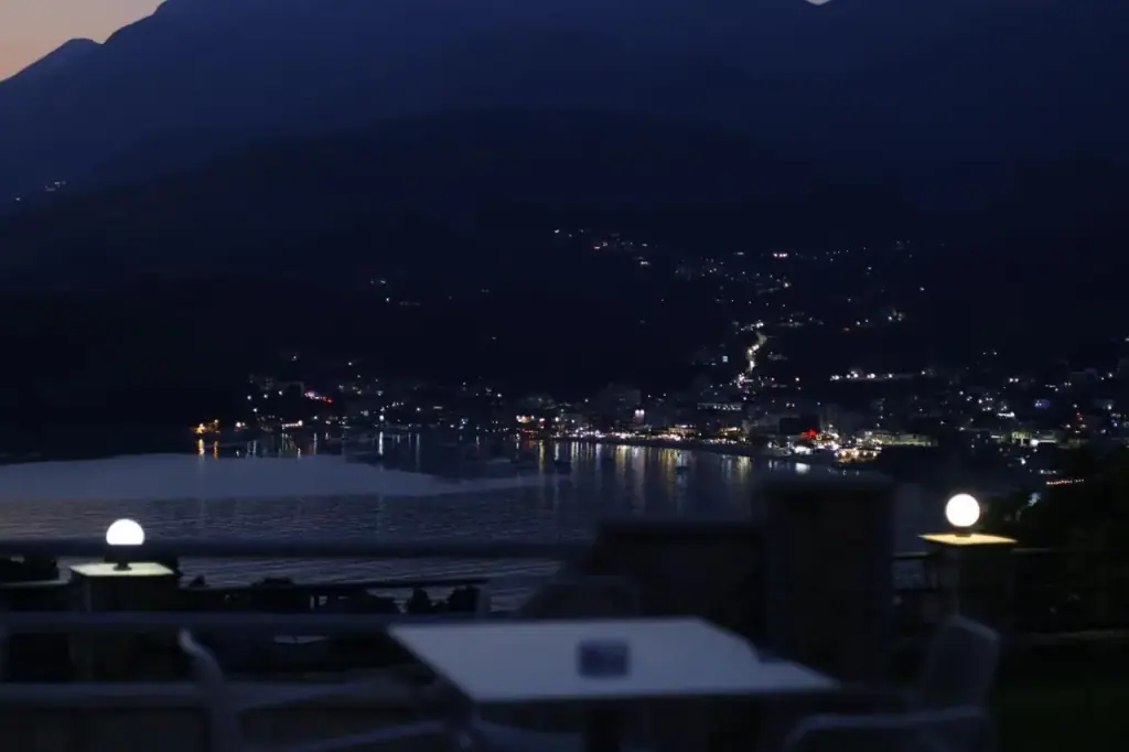 The terrace after dark with lamps on the stone wall and the lights of Himarë along the bay