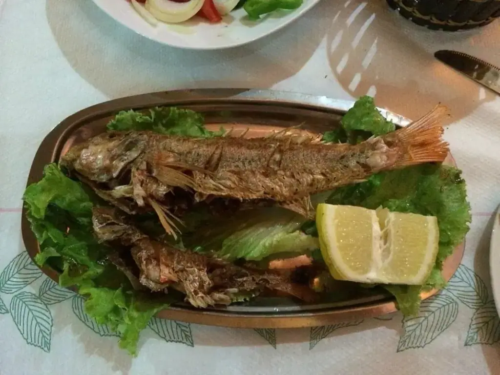 Whole fried fish on a copper platter with lettuce and two wedges of lemon