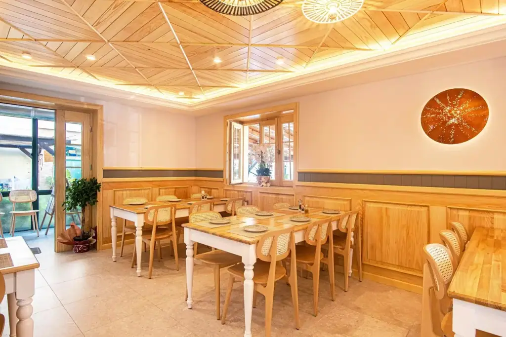 The dining room at Taverna Lefteri: pale timber panelling, a fitted geometric timber ceiling, cane-backed chairs and laid tables