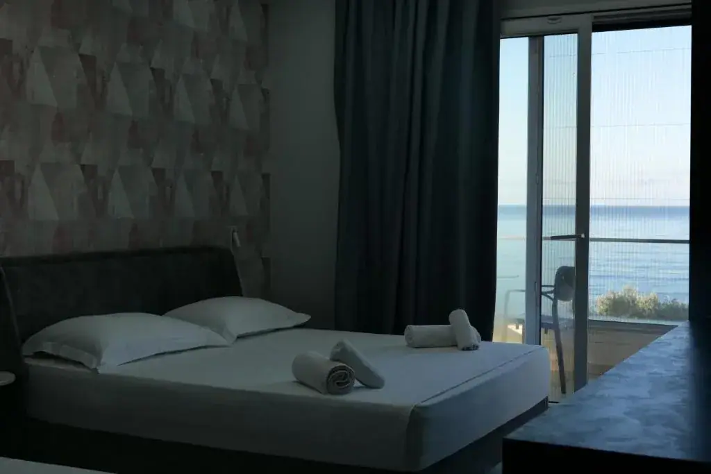 A room with a rose and grey triangle feature wall, a bed and a balcony door filled with open sea