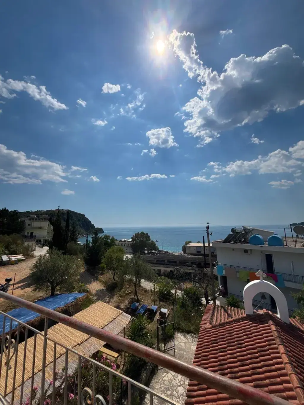 The view from a hostel balcony over tiled roofs and olive trees to the sea and a green headland