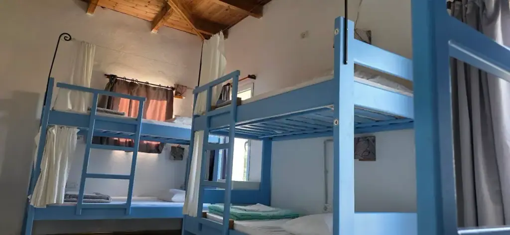 Numbered blue bunks with white curtains beneath an exposed timber roof