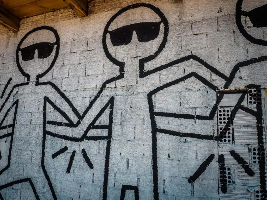 Close-up of the hand-painted mural of stick figures wearing sunglasses on a whitewashed block wall