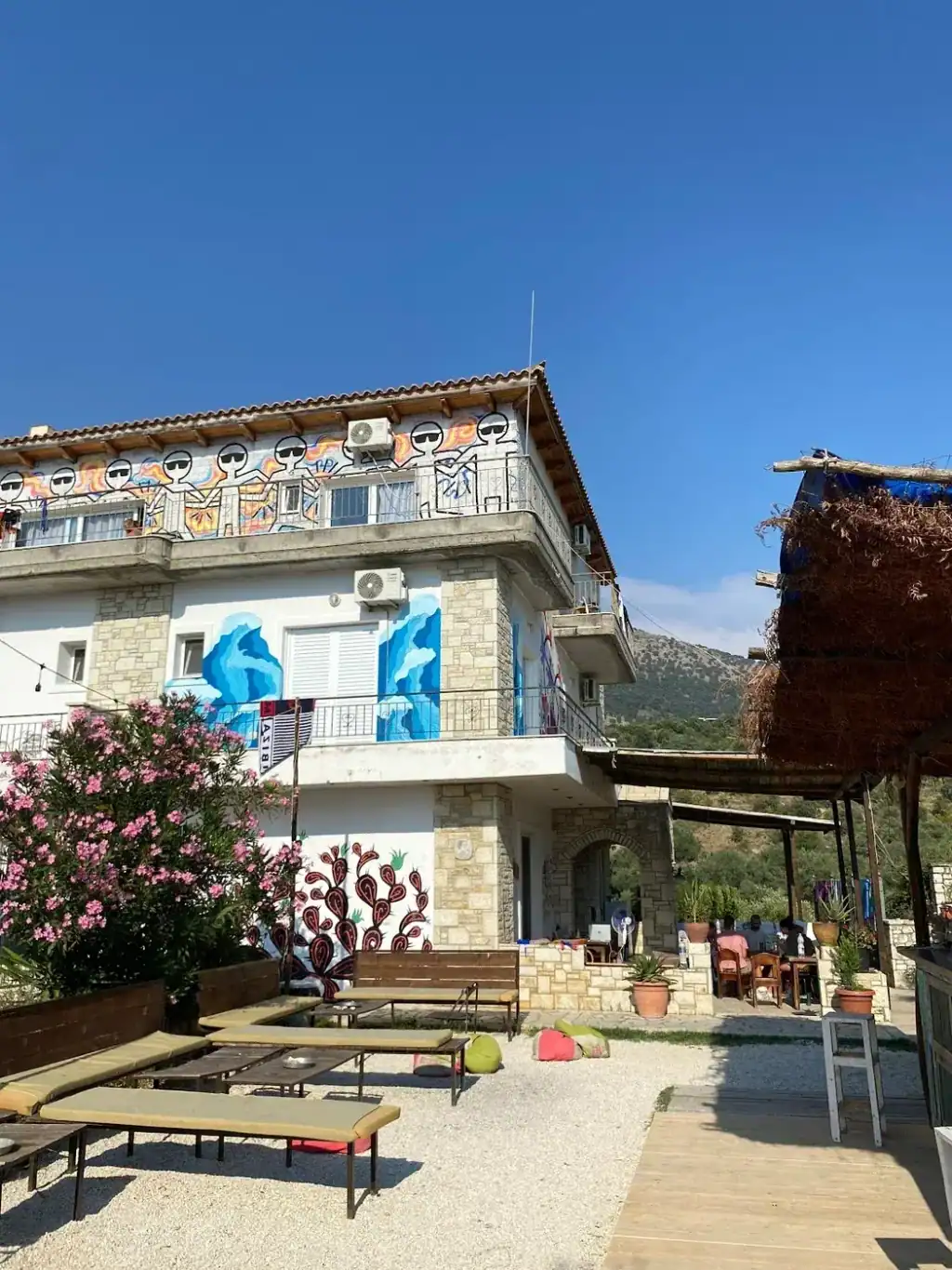 The three-storey villa at Trip'n'Hostel Seaside, its top balcony painted with black stick figures, seen from the gravel garden