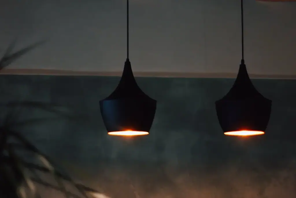 Two black pendant lamps hanging against UMI's blue-slate plaster wall, each throwing a small warm disc of light