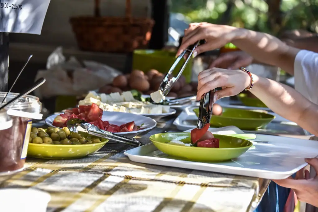 Hands serving tomatoes, cheese and olives from a breakfast table onto green plates and white trays
