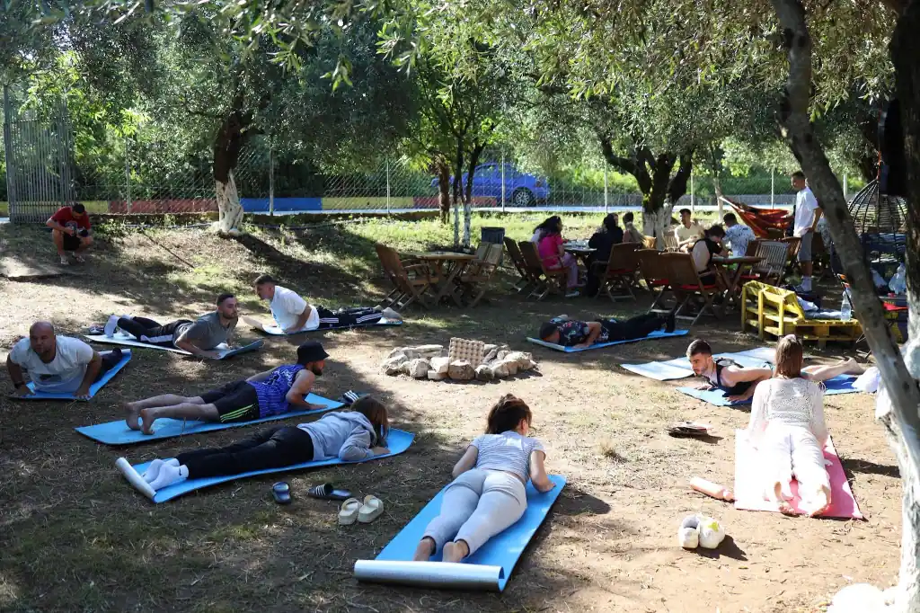 Guests stretching on blue mats in the shade of the olive grove, around a ring of stones for the fire