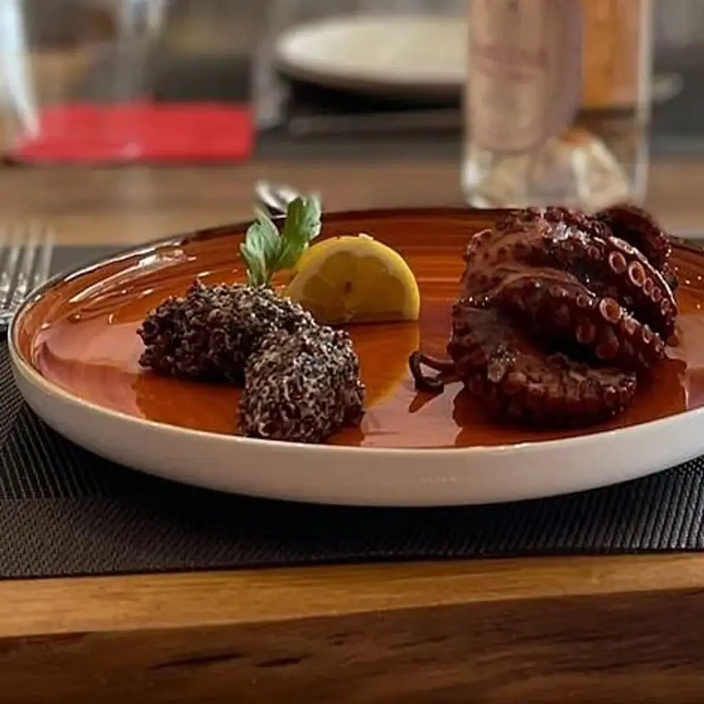 Grilled octopus with lemon and two dark croquettes on a copper-glazed plate, close