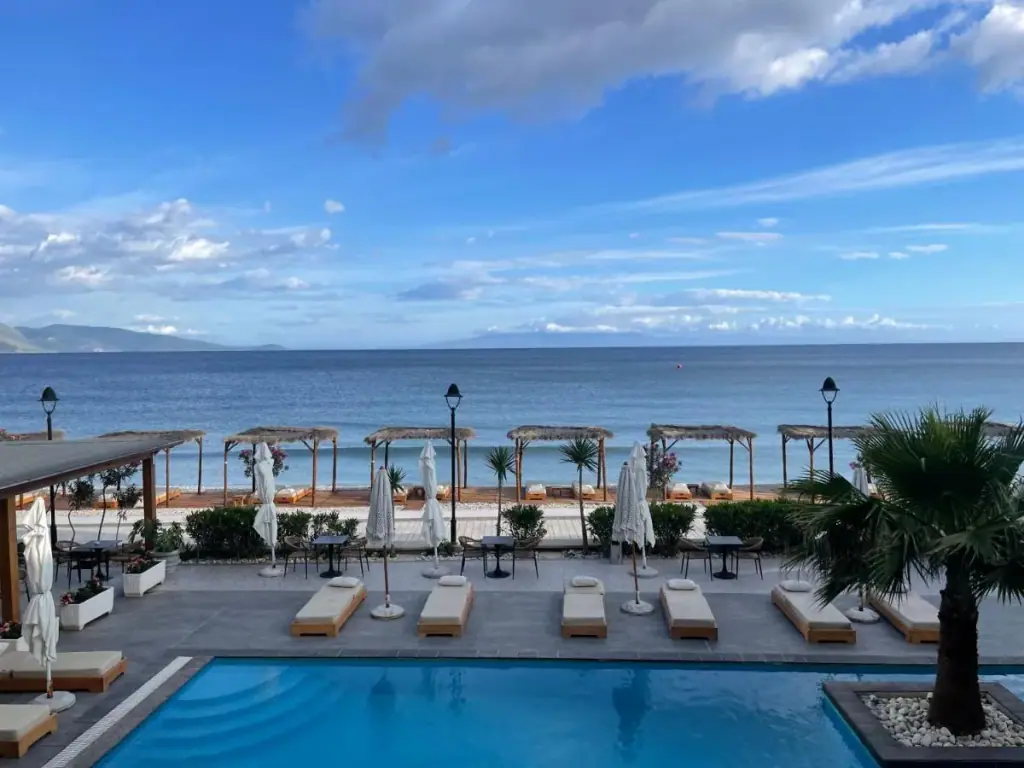 Loungers and folded parasols around the pool with the Ionian bay and the far headland beyond