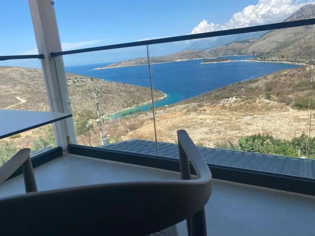 The inlet and the headland of Porto Palermo seen over a glass balcony balustrade
