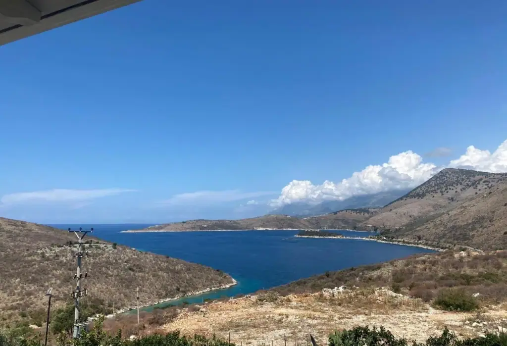 The bay of Porto Palermo seen from the property: a narrow green inlet in the foreground, the open Ionian beyond, bare hills either side