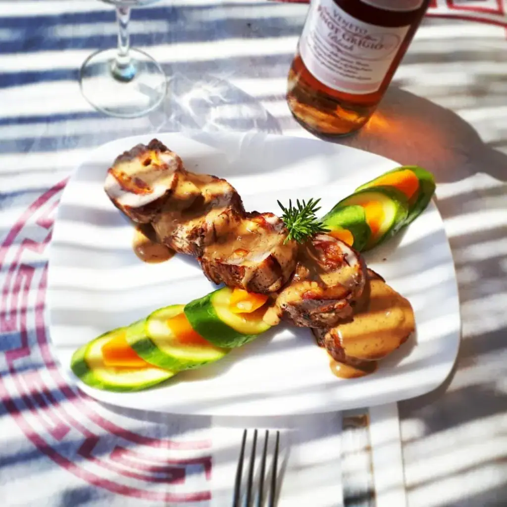 A white plate of grilled medallions in a pale sauce with sliced courgette and carrot