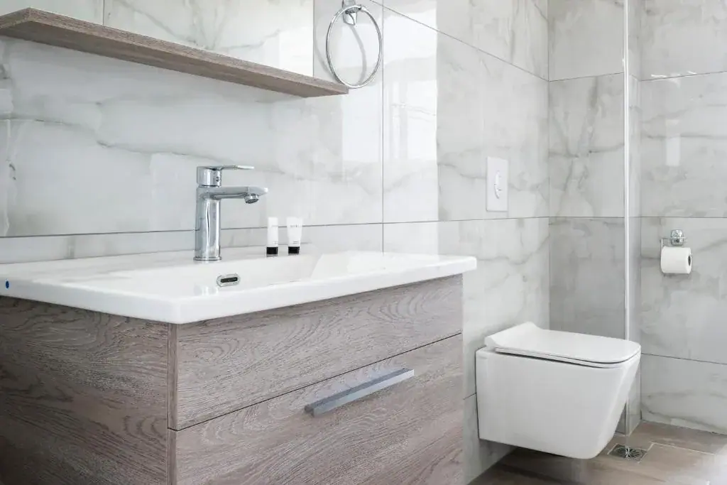 A white marble bathroom at Wait 'n Sea with an oak vanity, a wide rectangular basin, a wall-hung WC and a glass shower screen