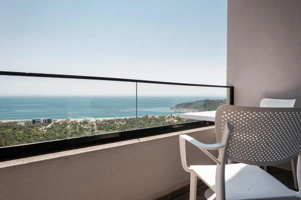 A balcony at Wait 'n Sea with a black-capped glass balustrade looking down over the wooded coastal plain to the open Ionian and a green headland