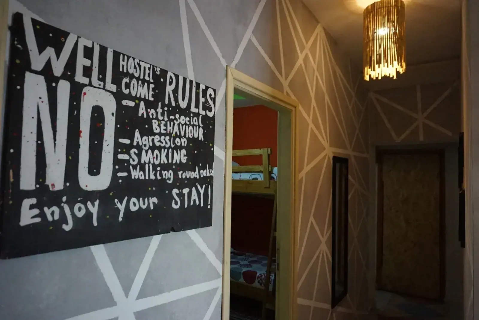 A hand-painted black board on a grey wall at Himara Downtown Hostel reading Wellcome, Hostel's Rules, No anti-social behaviour, aggression, smoking — enjoy your stay