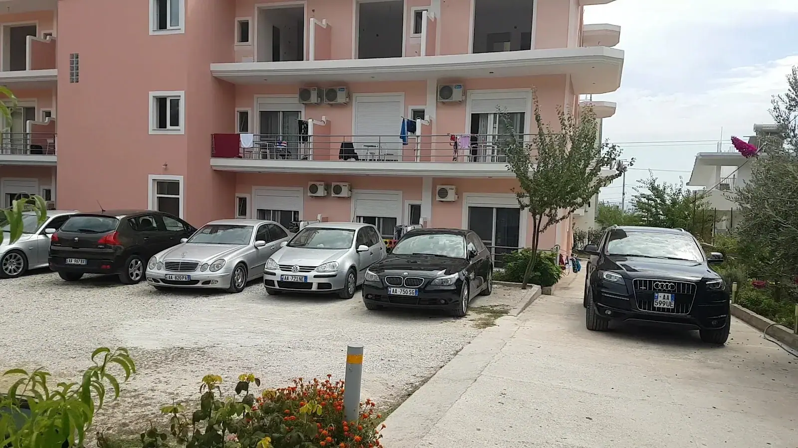 Cars parked on the hard standing in front of the hotel, balconies, roller shutters and wall air-conditioning units above