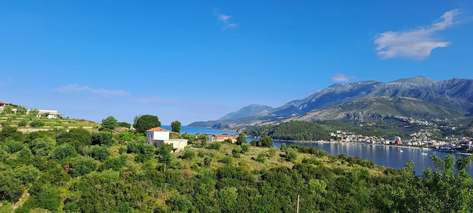 A wide view over green hillside terraces to a blue bay and the mountains behind it