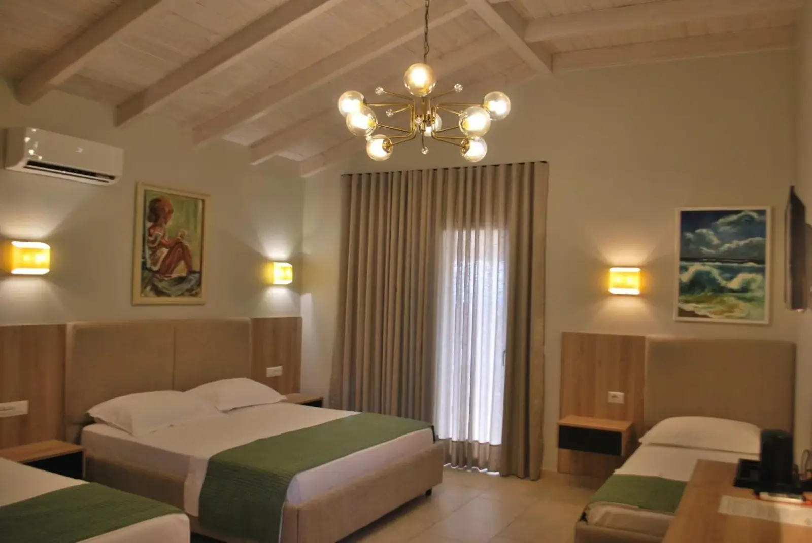 A room with a green bedspread, a boarded ceiling, a brass chandelier and a door to a balcony