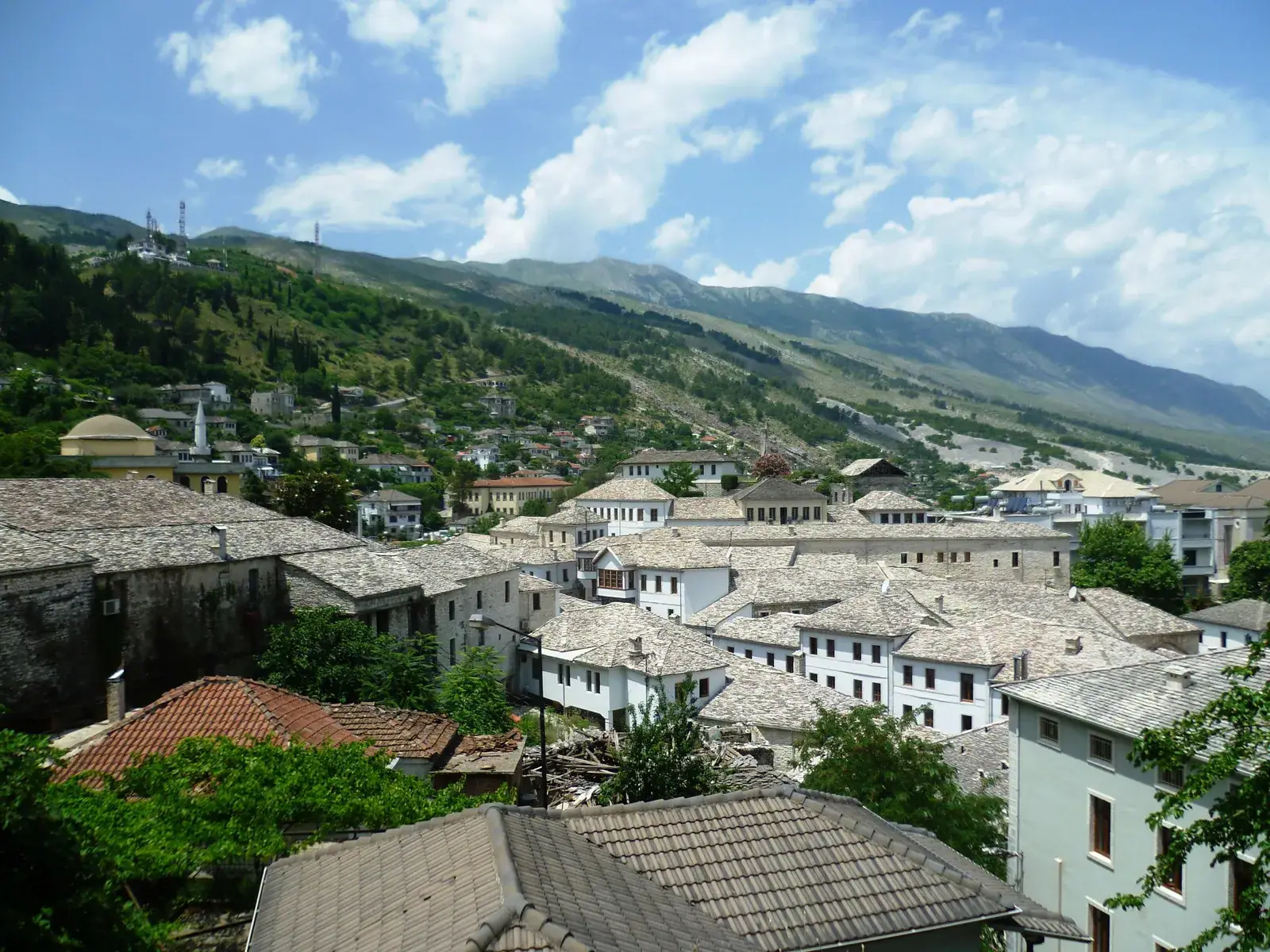 Grey slate roofs and white stone houses of Gjirokastër's old town spreading up a green hillside under a long mountain ridge