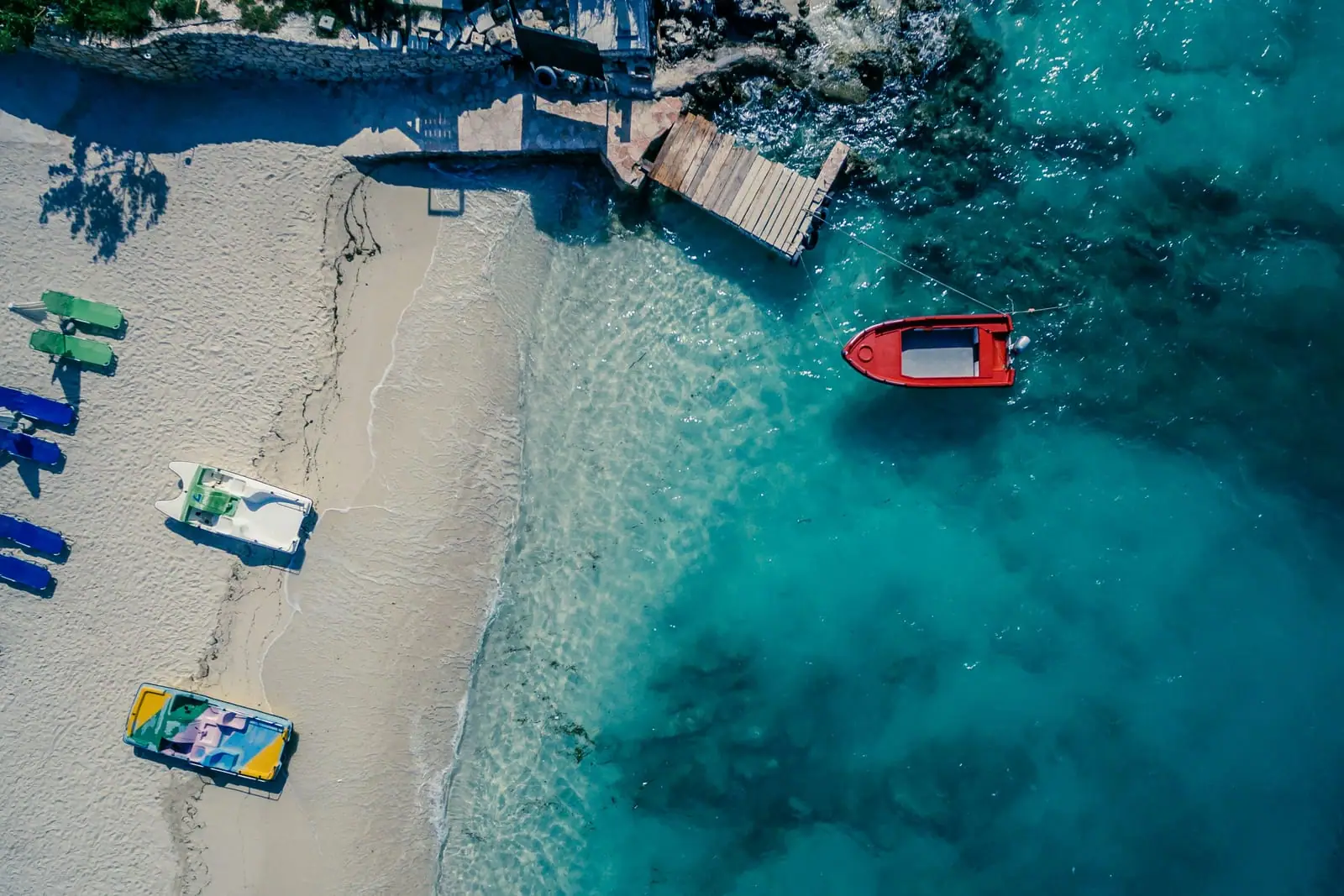 Quiet Ksamil cove, pedalboats on white sand and a red speedboat moored in turquoise water