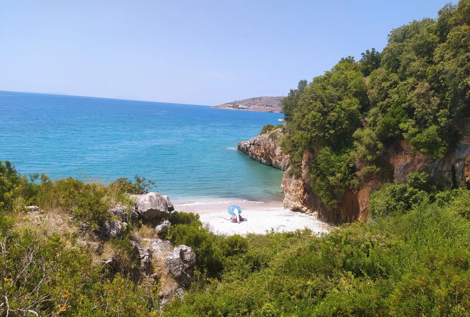 Qeparo Beach cove with sunbeds on the shingle and a wooded headland behind