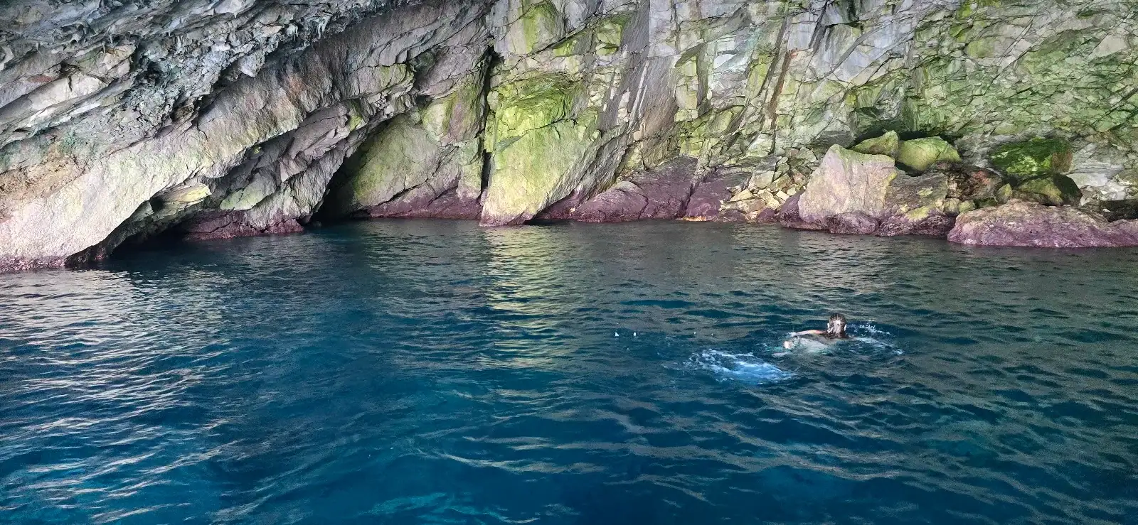 Streaked cliff wall dropping into deep blue water at Bats Cave