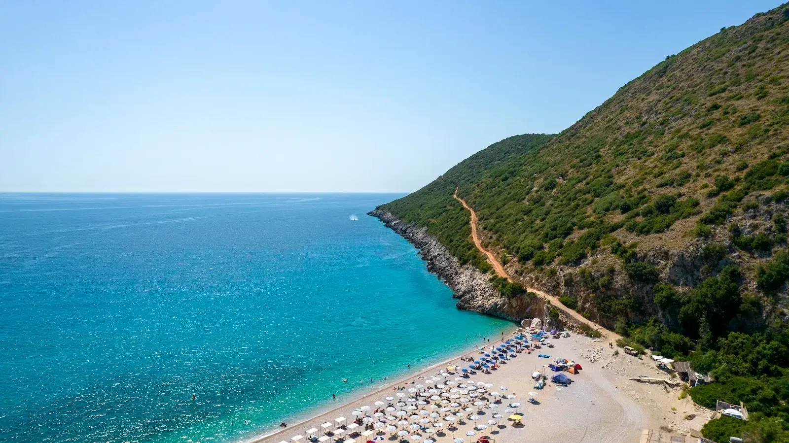 Gjipe Beach and its headland from above, umbrellas along the shore