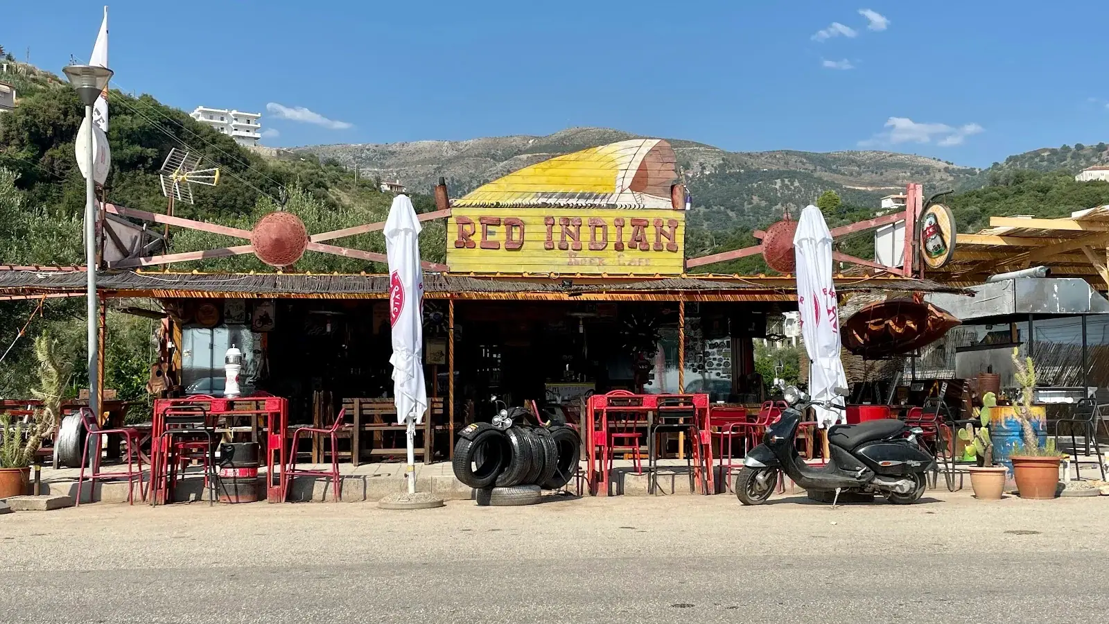 Rock-themed facade of Red Indian Rock Cafe with its painted sign and red chairs beside the highway