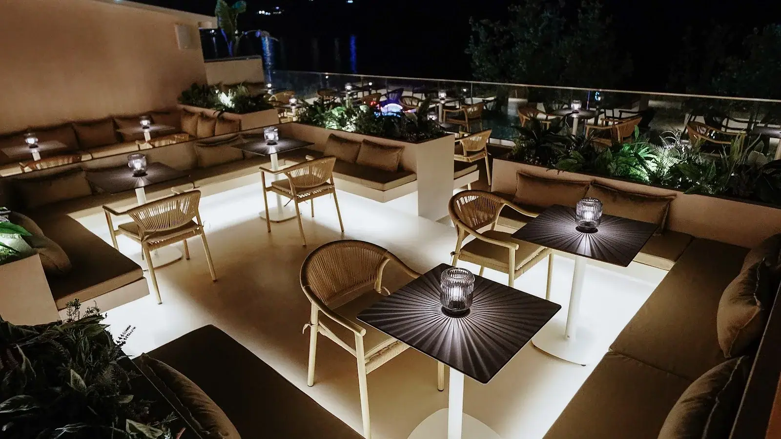Thèa Rooftop Bar terrace at night with lit tables, rattan chairs and softly lit sofas