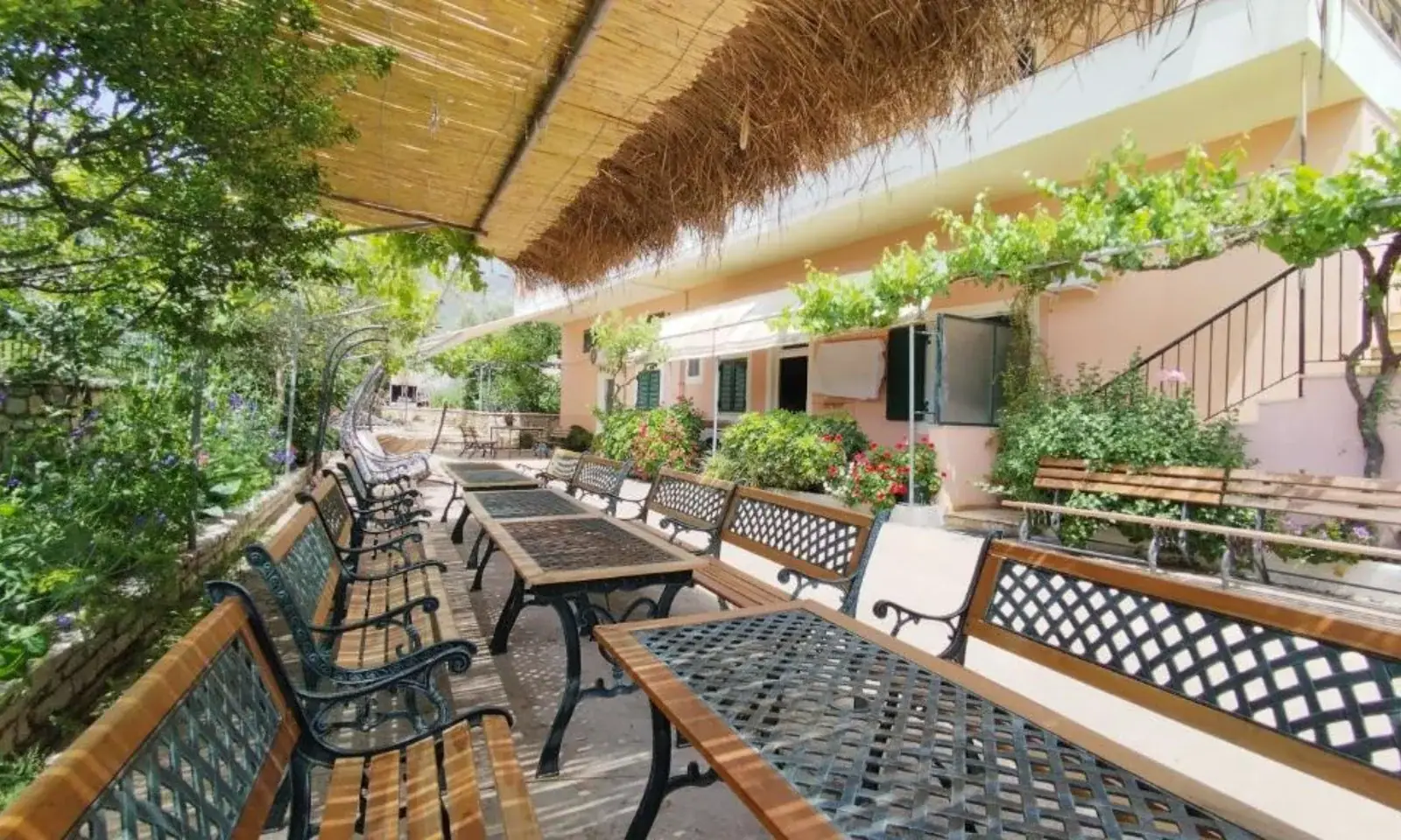 Shaded garden terrace with benches and communal tables at Oasis Hostel in Himara