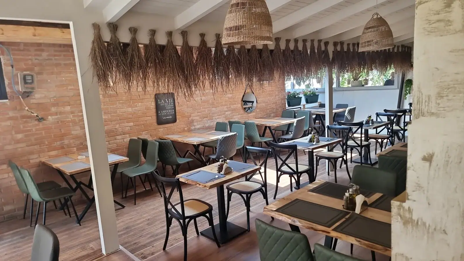 Rustic brick-walled interior with green chairs and set tables at Bocca Restaurant in Himara