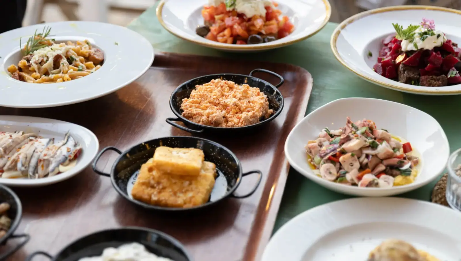 A painted table at The Jester's Taverna laid with plates of pasta, tomato salad, beetroot and marinated anchovies, pans of fried cheese and a coral-coloured dip, and a bowl of chopped octopus
