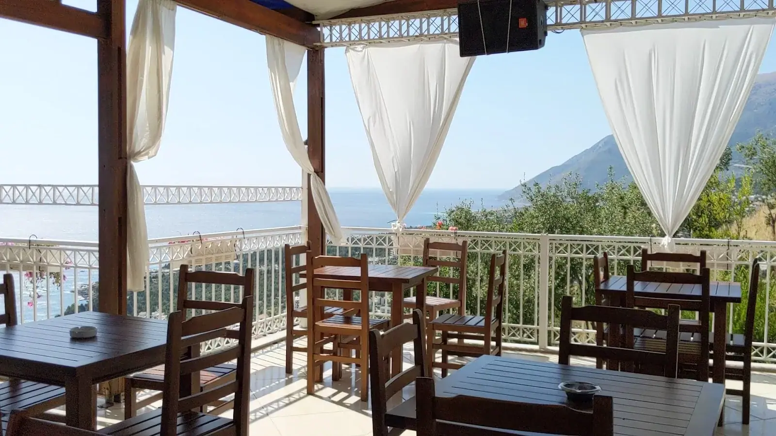 Rustic wood-beam dining room with set tables and plants at Panorama Restaurant on the Llogara Pass