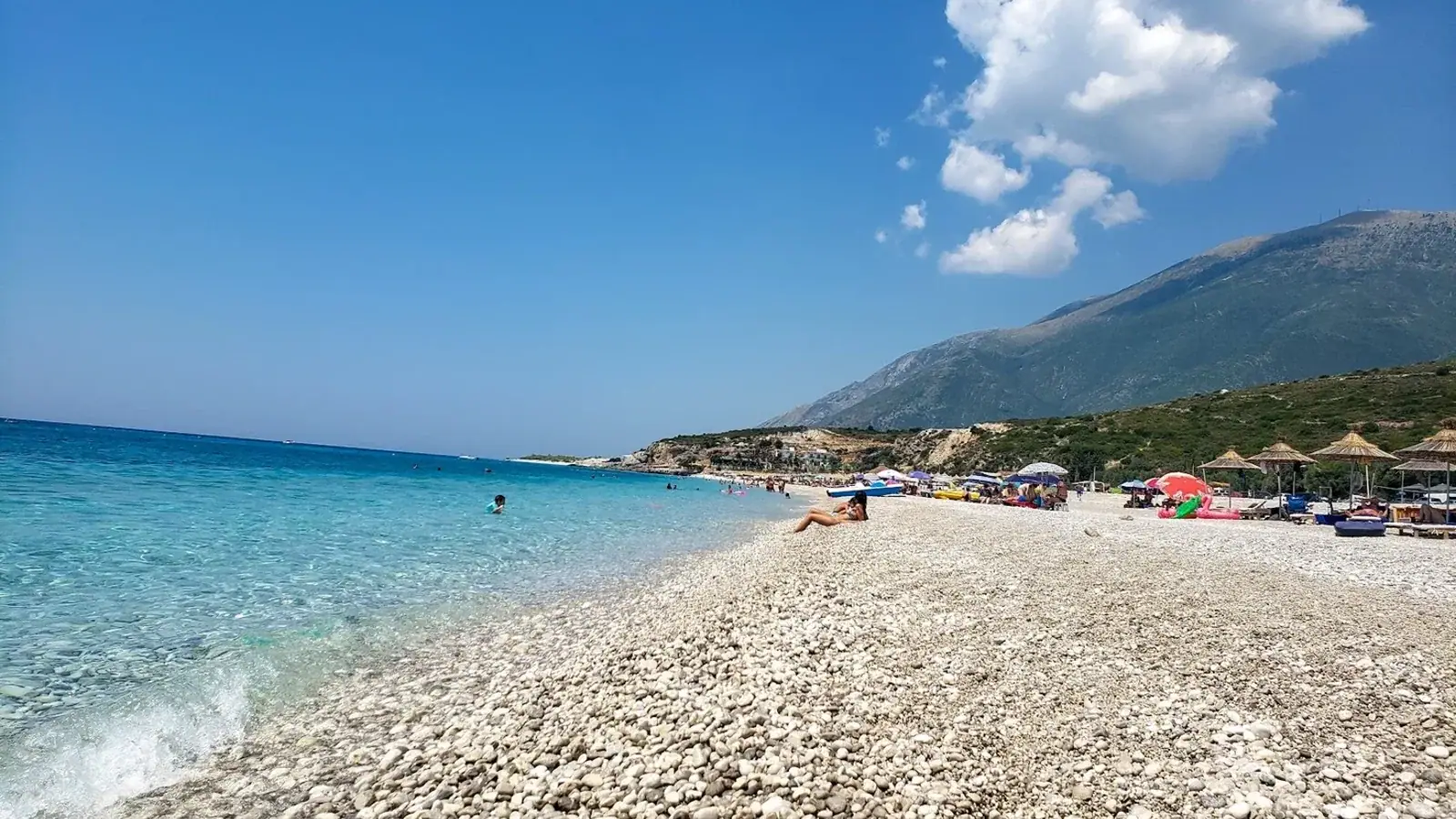 Dhërmi's long pebble beach below steep mountain slopes with deep blue water offshore