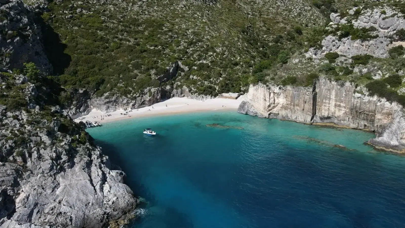 Aerial view of a turquoise cove with a boat and white-pebble beach on the Albanian Riviera near Himara