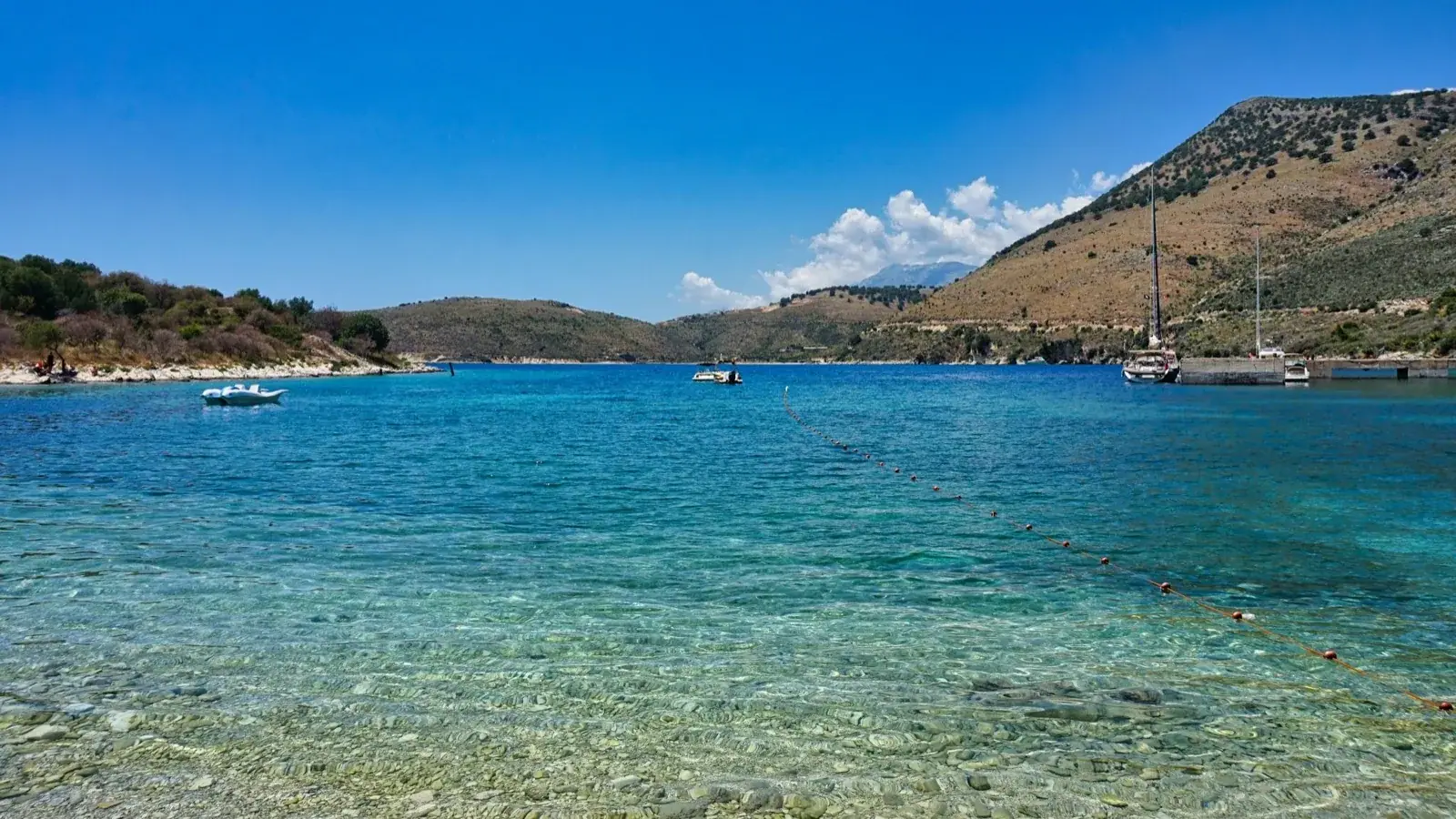 Small boats and a yacht moored off a shallow, clear-water bay on the Albanian Riviera