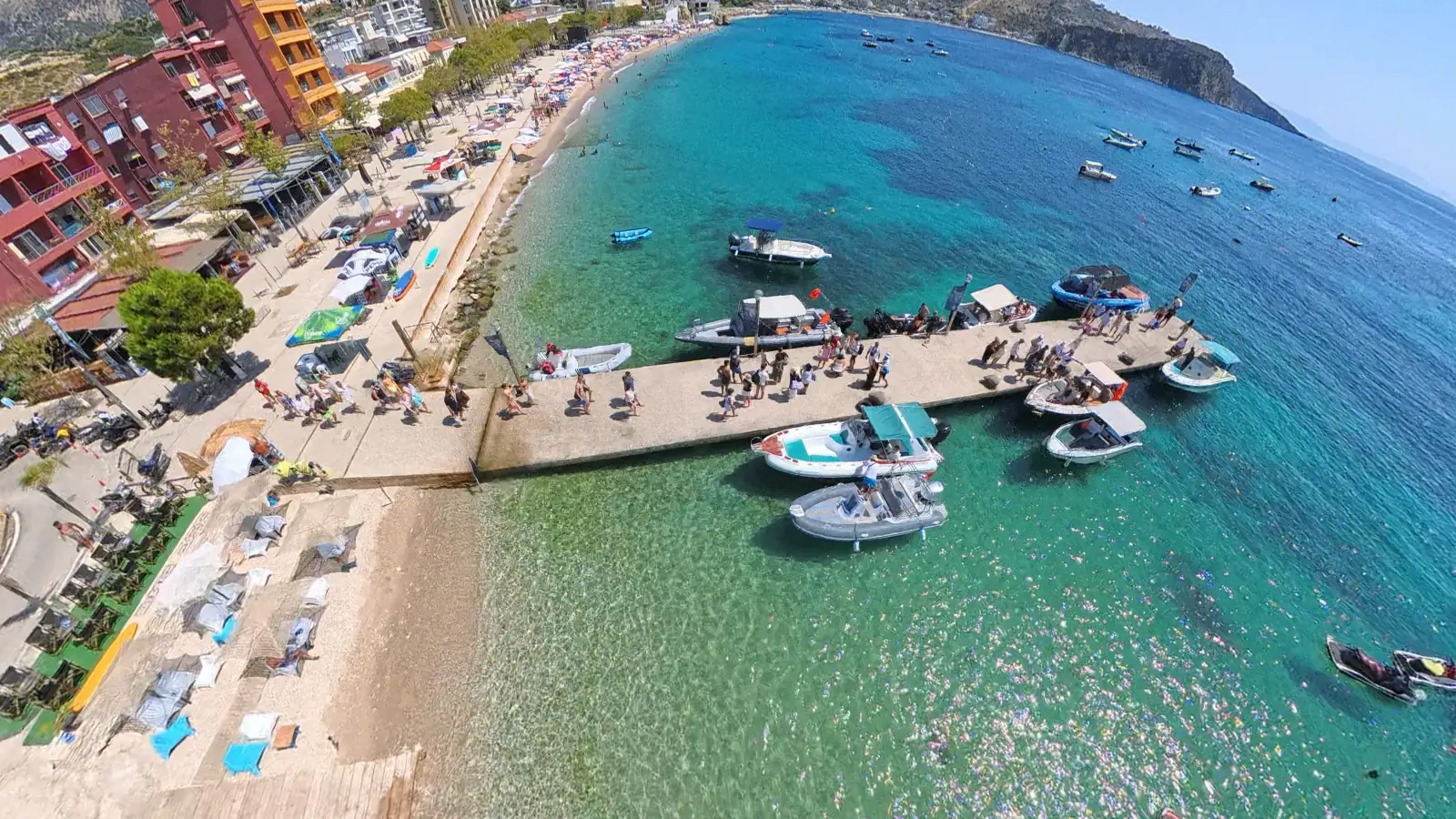 Aerial view of Himara Mini Dock with tour boats moored along the pier and Spile Beach curving behind