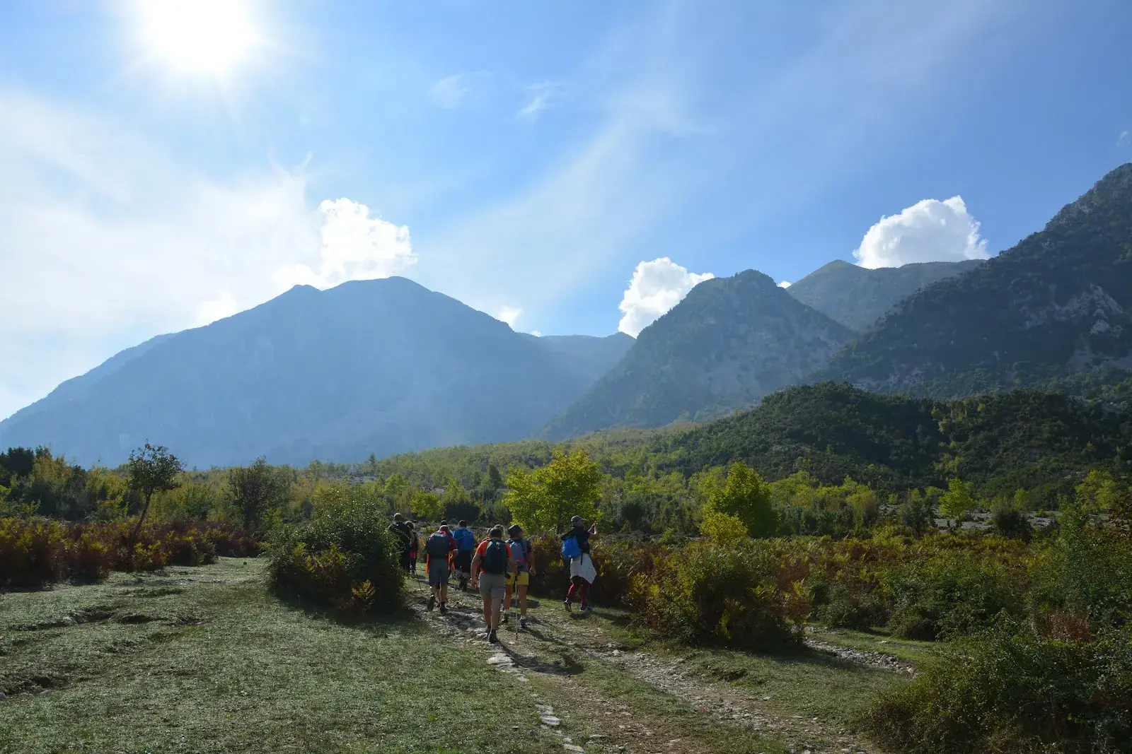 Walkers on a grass track heading toward the ridge of Mali i Bogonicës inland from Himara, autumn bracken either side and bare limestone summits ahead
