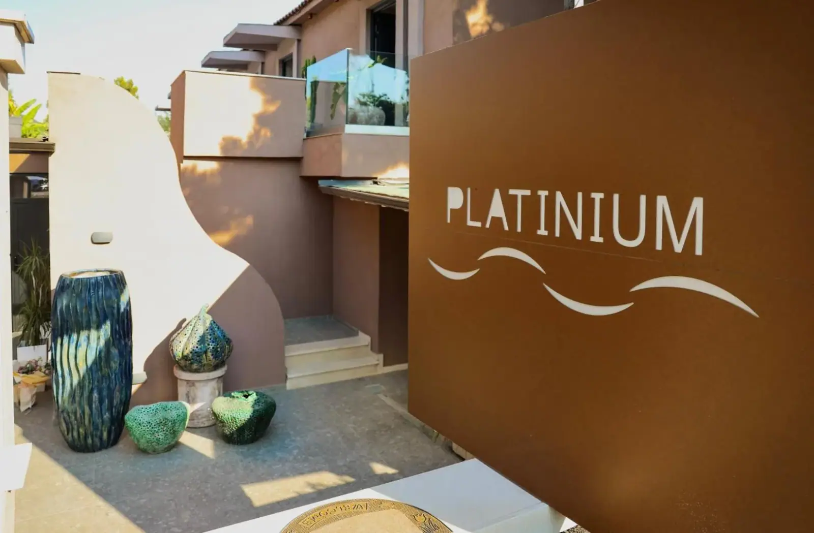 The word PLATINIUM in white with a wave device, painted on a rust-coloured wall beside a curved white wall and glazed vases