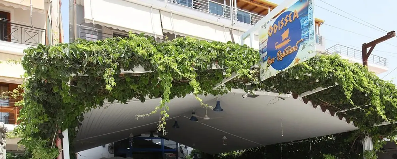 The creeper-covered pergola over the front of Restaurant Odissea, with the round Odissea Bar-Restorant sign above it