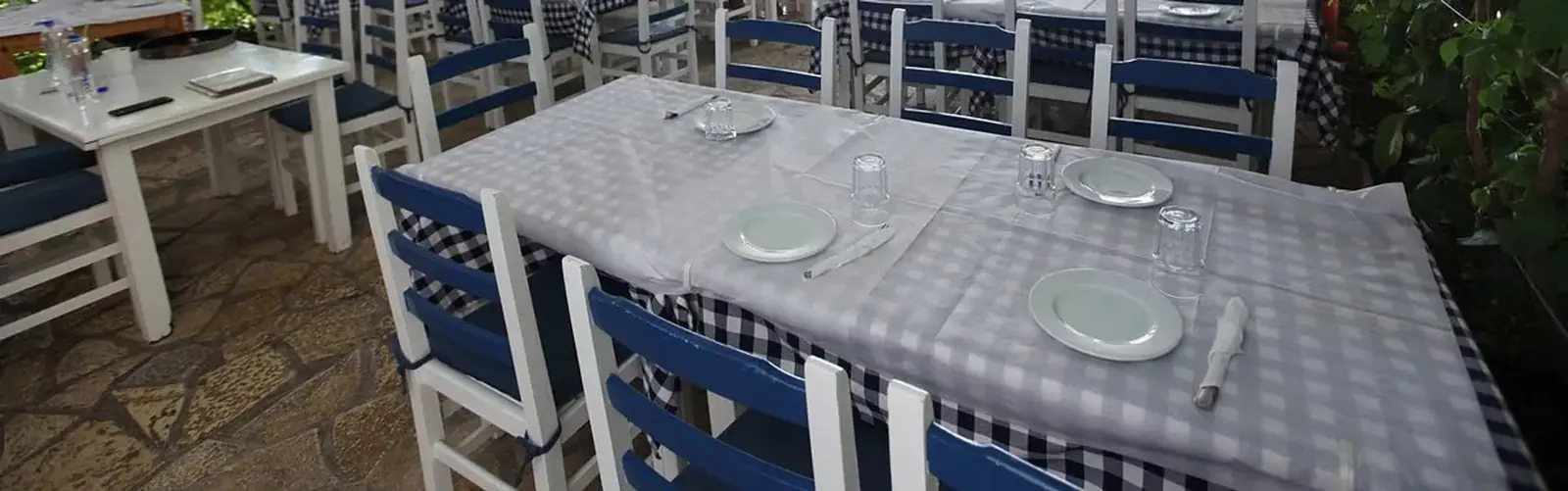 Laid tables and blue-and-white painted timber chairs on the flagstone terrace, gingham cloths over the chair backs