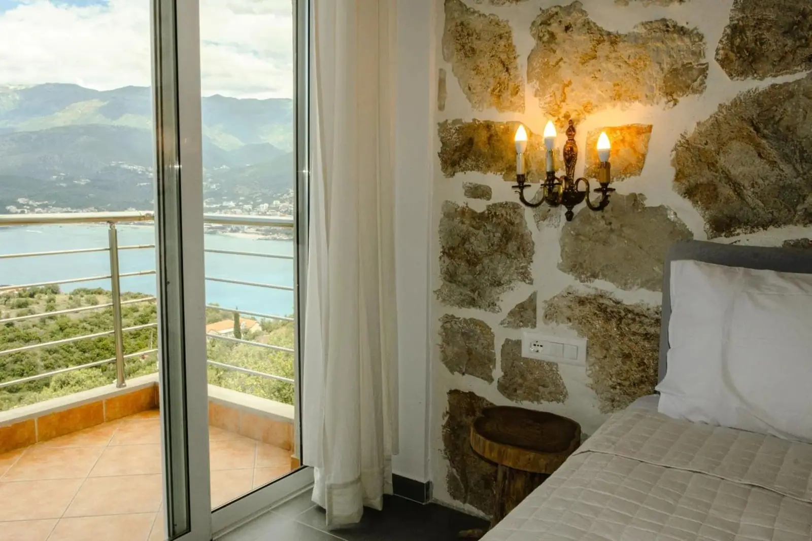 A room with a stone feature wall and a wrought-iron candelabra beside a sliding door onto a balcony over the bay