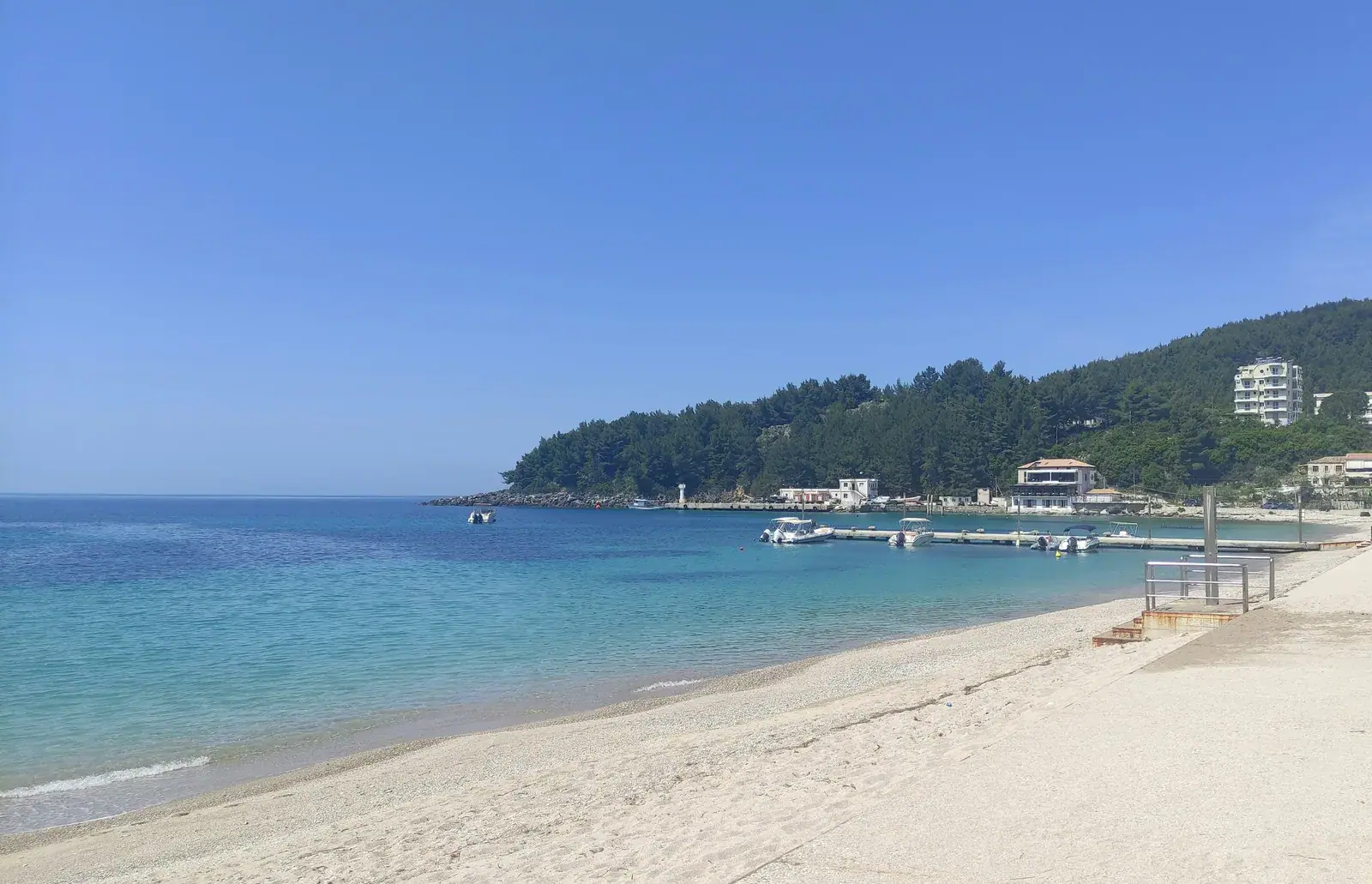 Spile bay in Himarë, its jetty and the pine headland — the town the restaurant stands in, not the restaurant