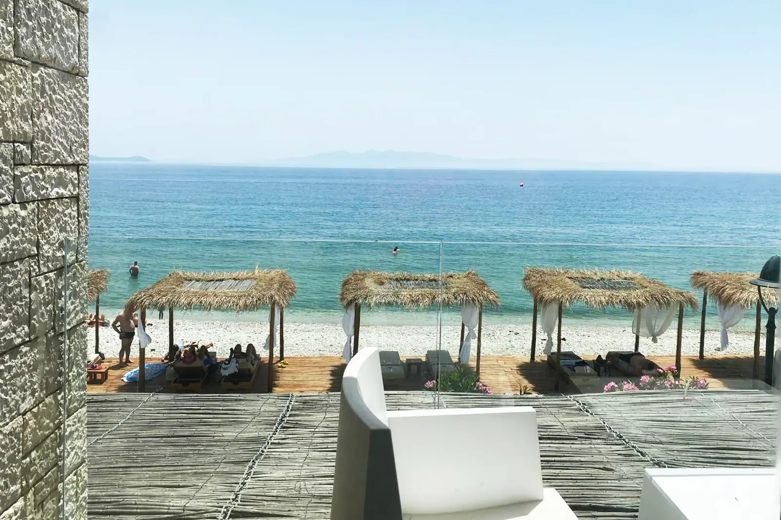 Flat thatched canopies hung with white curtains standing over loungers on the timber deck at the water's edge