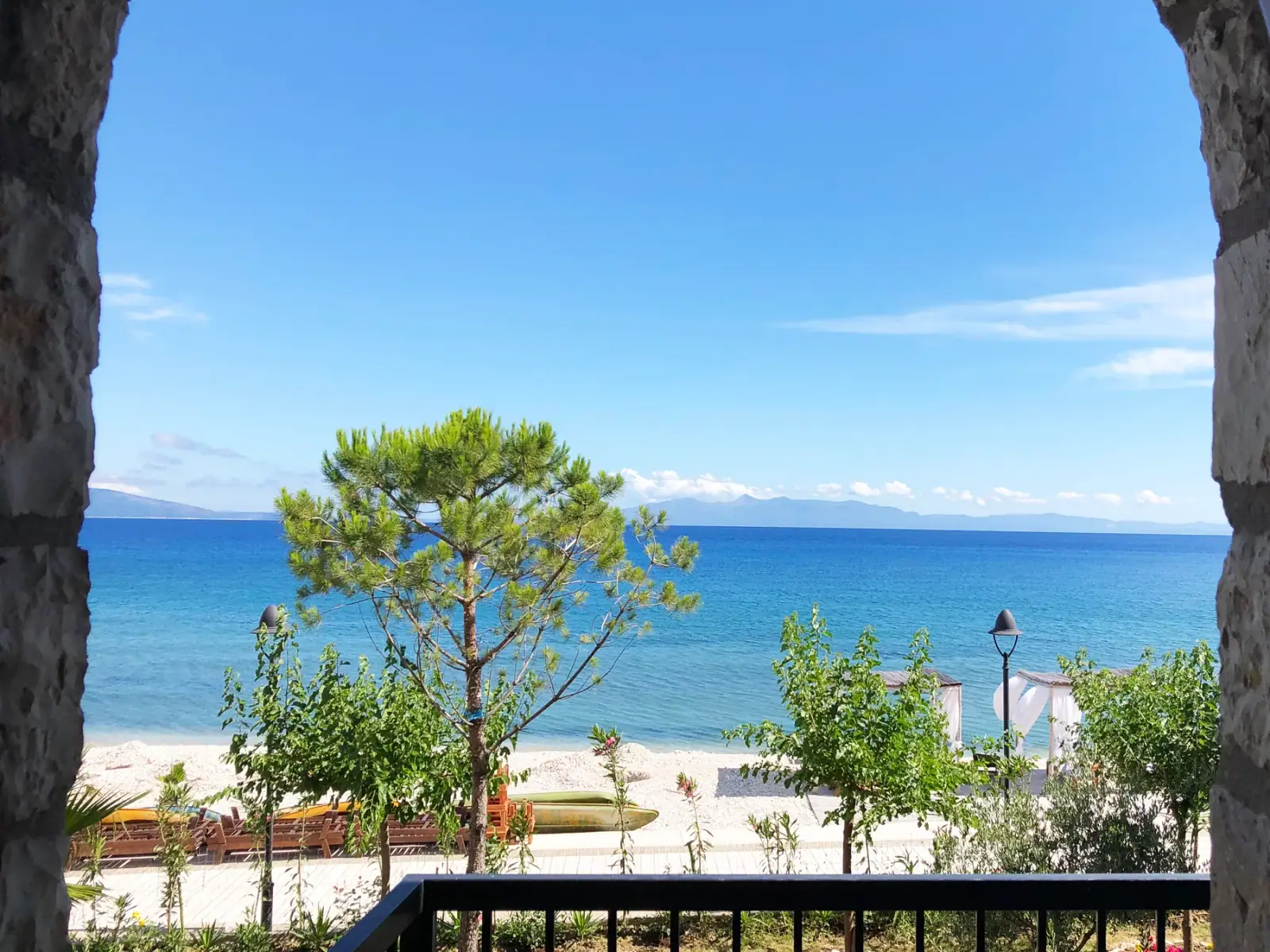 The beach and the bay seen from a room balcony, past a single pine on the shore frontage