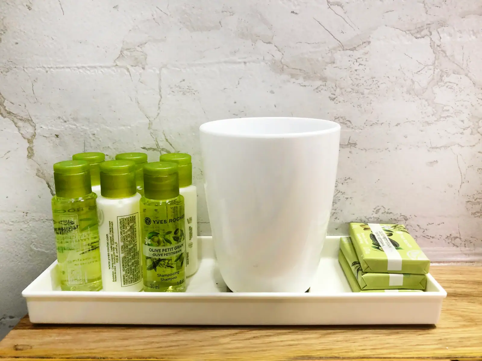 A tray of six green toiletry bottles and two wrapped soaps beside a tall white beaker