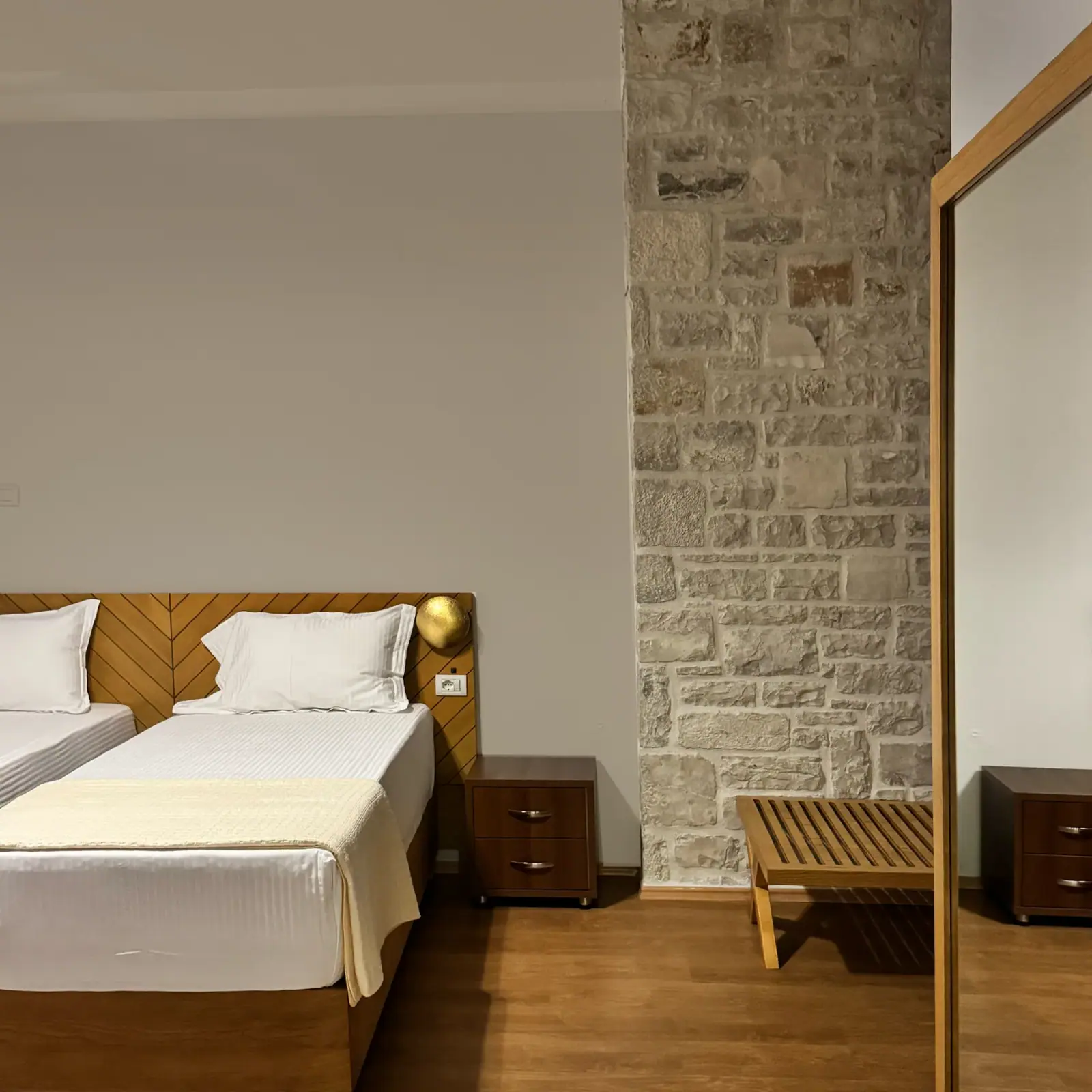 Beds with a timber chevron headboard beside a limestone pier, a slatted bench and a mirrored wardrobe