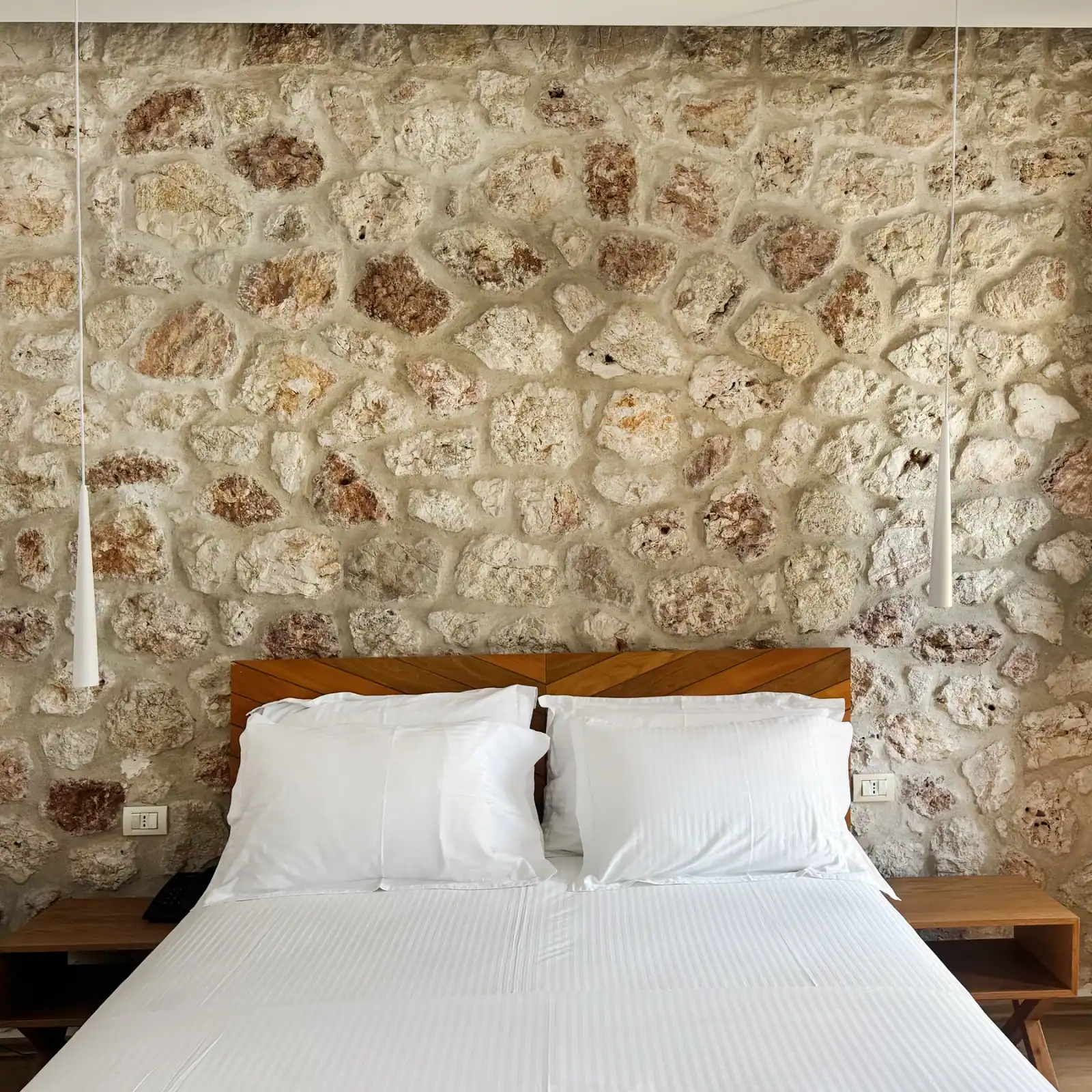 A double bed with a timber chevron headboard against rough limestone