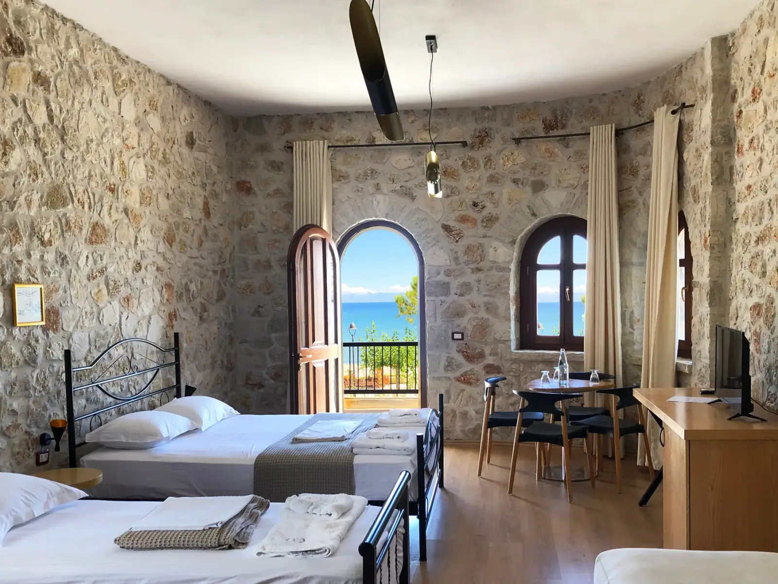 A stone-walled room with an arched window over the sea, a round table and four chairs