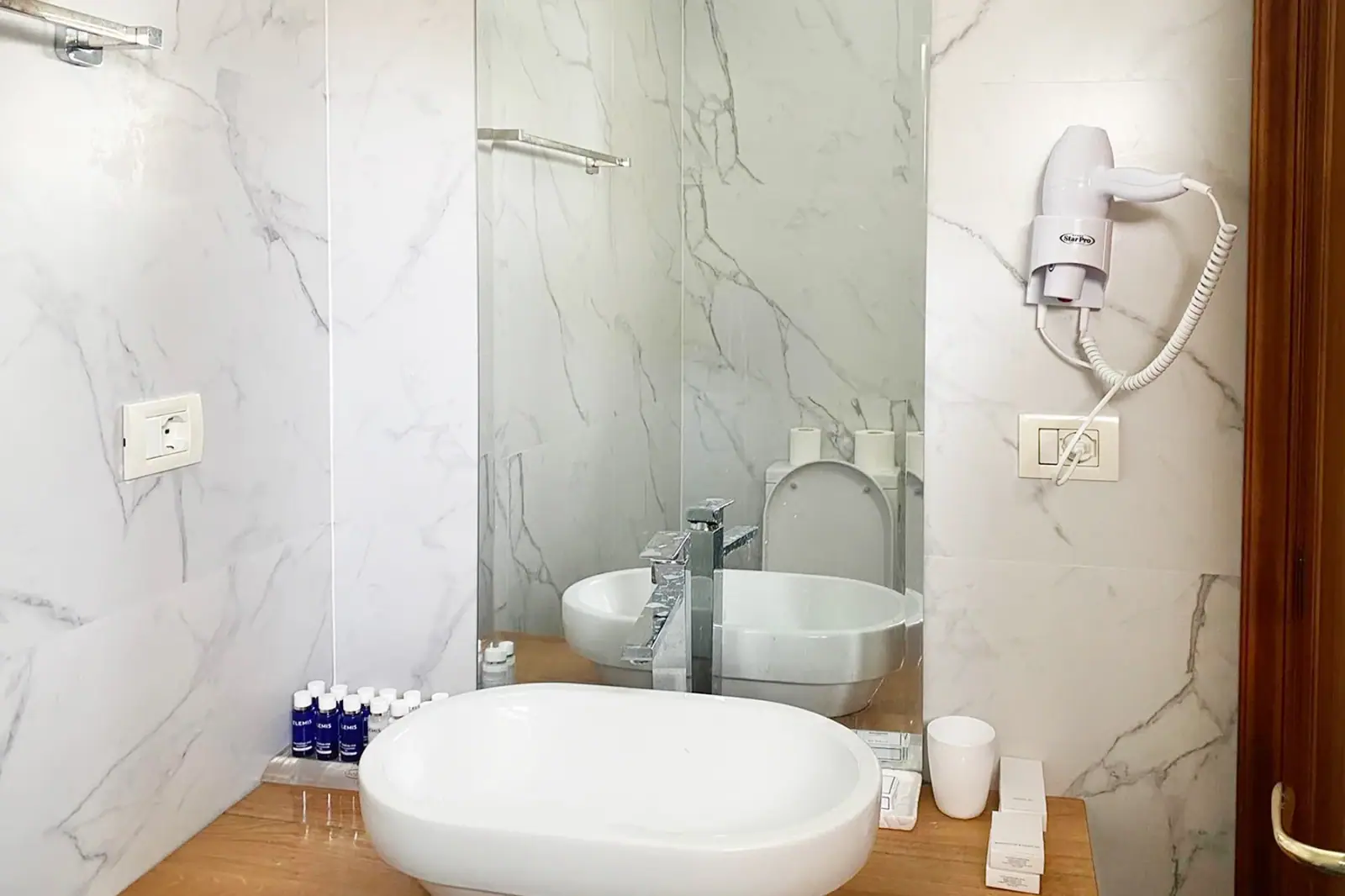A wide white oval basin on a timber shelf in a marble bathroom, its mirror behind